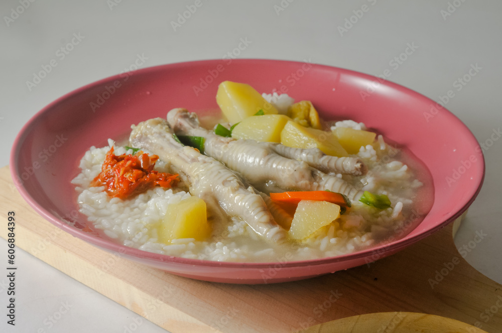 White rice with chicken leg soup and chili sauce served on a red plastic plate on a wooden cutting board isolated on a white background White rice with chicken leg soup and chili sauce served on a red plastic plate on a wooden cutting board isolated on a white background