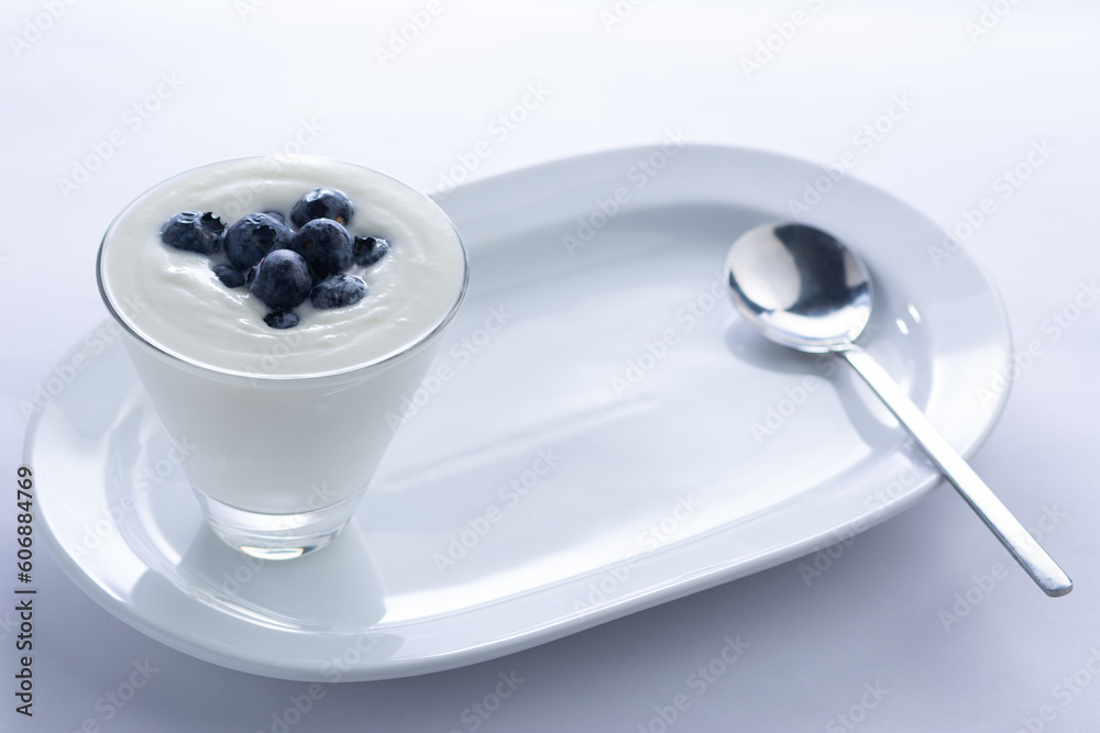 Yogurt and blueberries in a glass sitting on a white ceramic plate with a spoon Yogurt and blueberries in a glass sitting on a white ceramic plate with a spoon