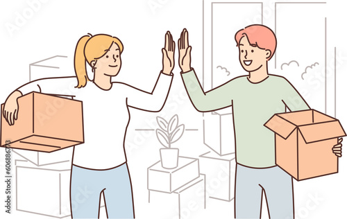 Happy married couple moving into new house and giving each other high five standing with boxes