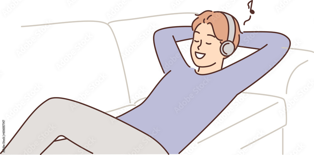 Φωτογραφία Man listens to music lying on couch with headphones and enjoys cool audio sound