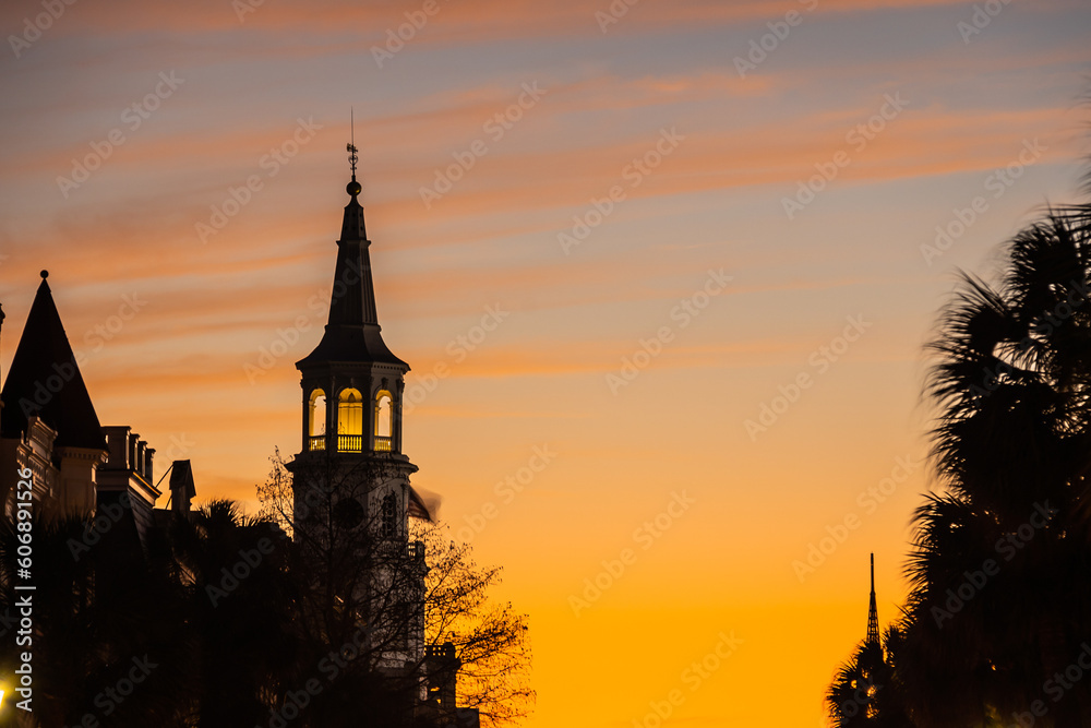 The steeple of a church in silhouette against the warm colors of a sunset on the clouds and the cool colors of the blue sky.