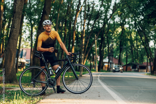 Cycling man standing next to his bike during a break and using a smartphone