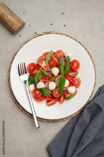 Salad with cherry tomatoes and mozzarella in a white plate on a gray background