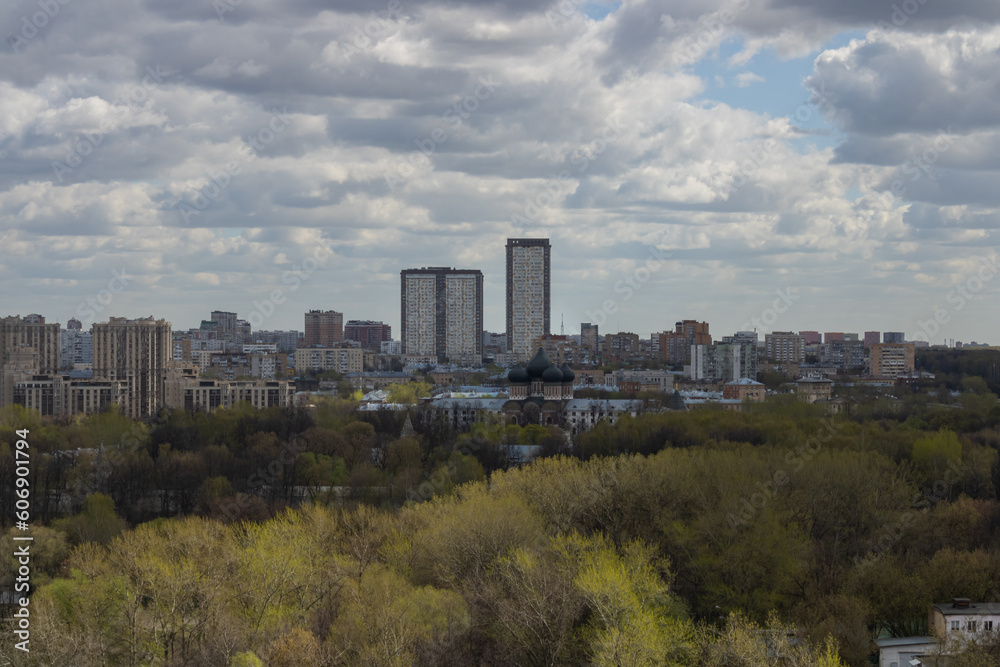 Panorama of Moscow. Park, trees with young leaves, church with black domes, houses. The beginning of spring in Moscow. Cloudy sky.