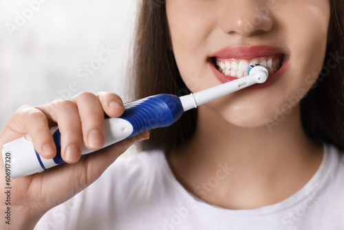 Woman brushing her teeth with electric toothbrush indoors  closeup