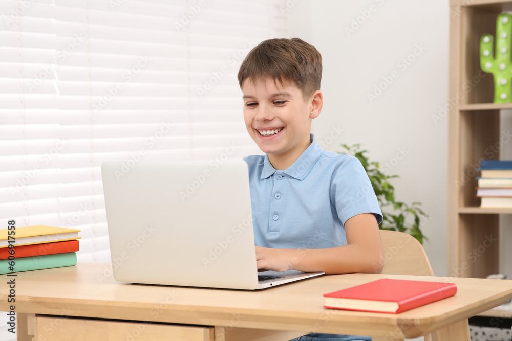 Smiling boy using laptop at desk in room. Home workplace Smiling boy using laptop at desk in room. Home workplace