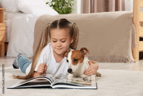 Cute girl reading book on floor with her dog at home. Adorable pet