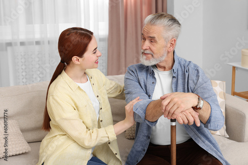 Caregiver and senior man with walking cane on sofa at home
