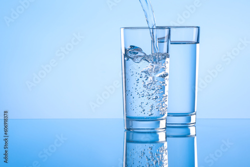 Pouring water into glass on light blue background. Space for text