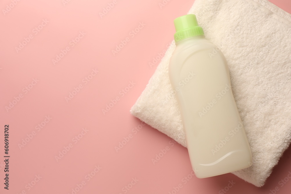 Bottle of fabric softener and terry towel on pink background, top view. Space for text Bottle of fabric softener and terry towel on pink background, top view. Space for text
