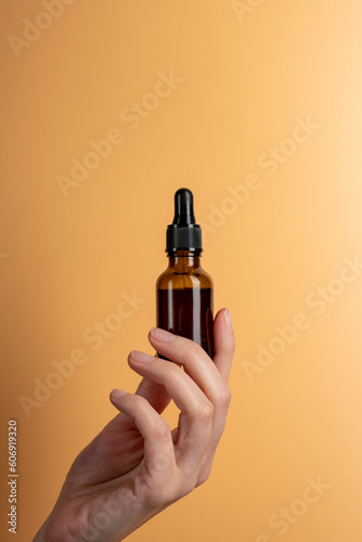 Female hand hold a brown glass bottle of care cosmetics on beige background. The concept of beauty products.