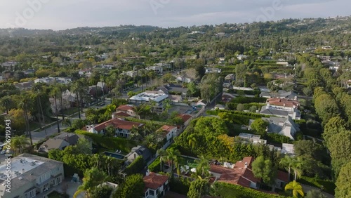 Fly above rich residencies in Beverly Hills at golden hour. Streets lined with rows of trees.
