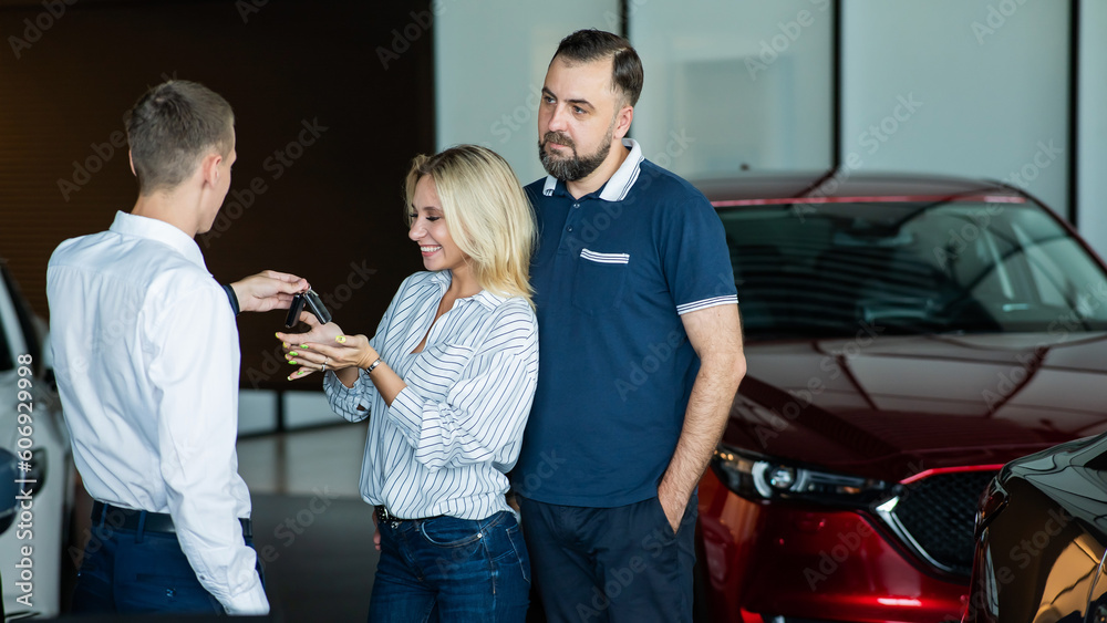 Obraz premium The seller hands over the car keys to the buyers. The couple bought a new car.
