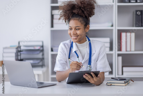 Happy doctor Portrait of young African American woman nurse or doctor smilingusing a laptop writing content at consultation photo