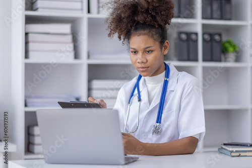 Happy doctor Portrait of young African American woman nurse or doctor smilingusing a laptop writing content at consultation
