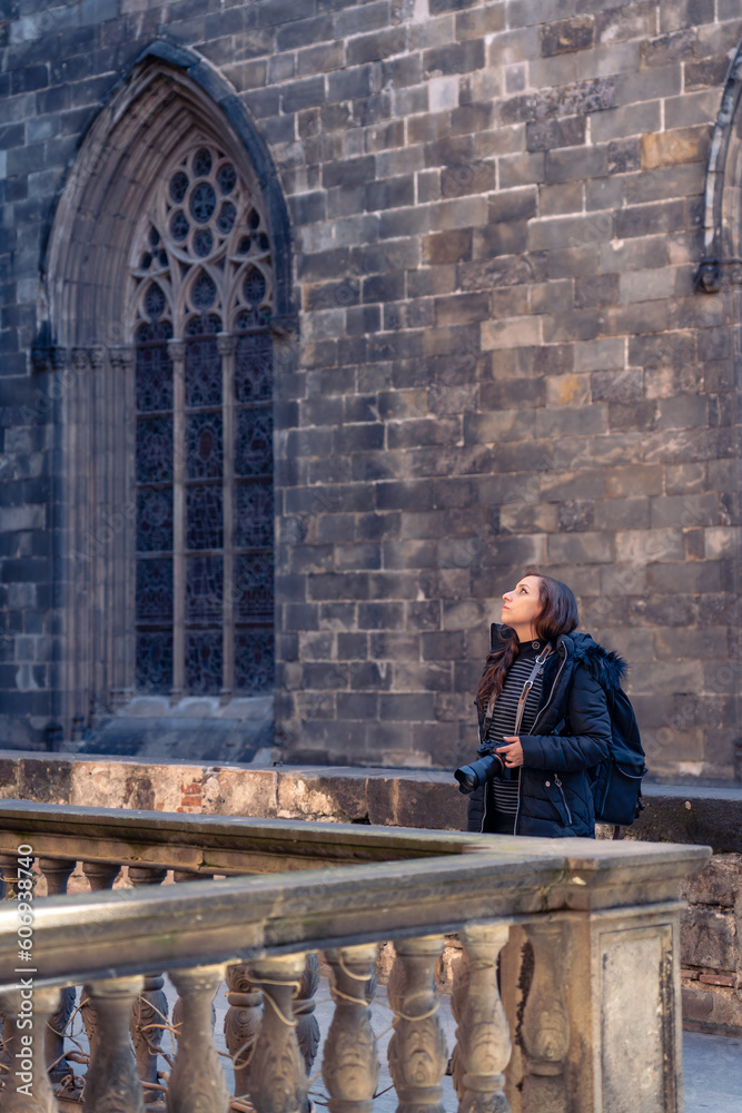 Thoughtful young woman tourist with camera admiring old Barcelona Cathedral in Gothic Quarter while standing against brick wall during sightseeing trip in Spain Thoughtful young woman tourist with camera admiring old Barcelona Cathedral in Gothic Quarter while standing against brick wall during sightseeing trip in Spain