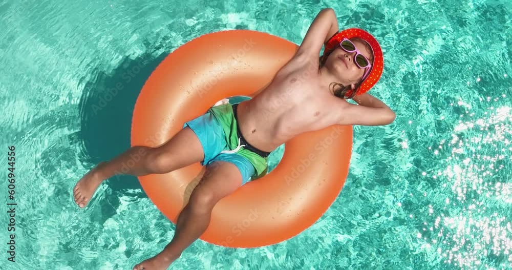Summertime fun. Pretty little kid swimming in pool. Aerial top view of kid in swimming pool from above, relax swim on inflatable ring. ummer vacation concept. Family beach summer vacation.