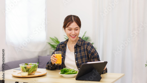 Lifestyle in living room concept, Young Asian woman touching on tablet and drinking orange juice