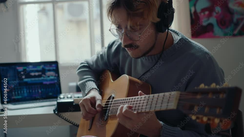 Young talented musician in headphones playing the guitar and enjoying music when working at home recording studio. Medium shot, focus on foreground