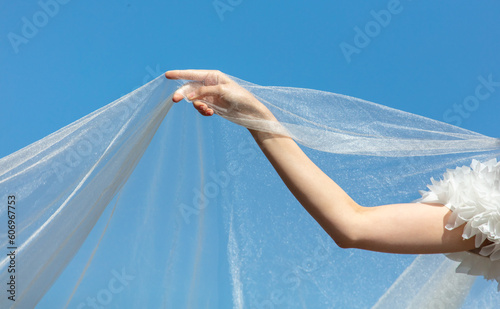 A woman's hand with a white wedding veil against a blue sky