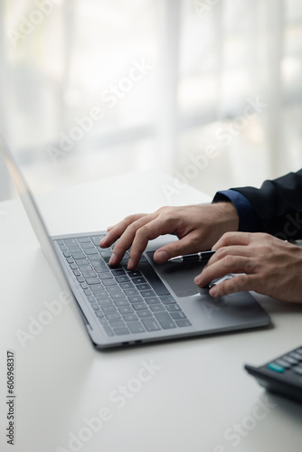 Person typing on laptop keyboard, businessman working on laptop, he is typing messages to colleagues and making financial information sheet to sum up the meeting.