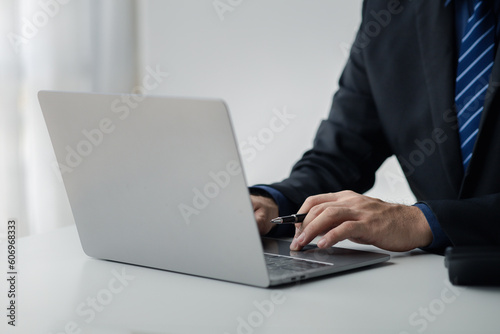 Person typing on laptop keyboard, businessman working on laptop, he is typing messages to colleagues and making financial information sheet to sum up the meeting. © PhotosD