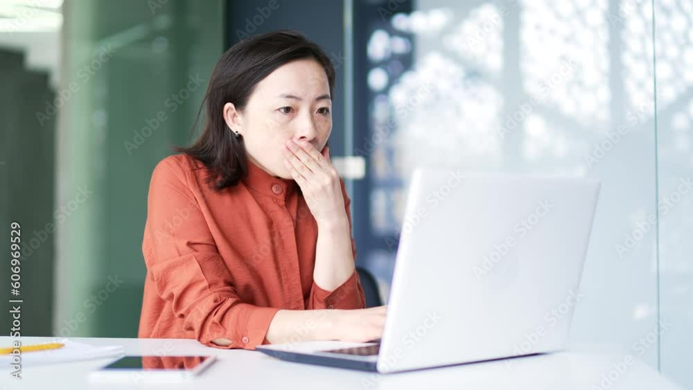Sad shocked asian businesswoman reading bad news on laptop computer while sitting at workplace in modern office. A female employee is disappointed by a notification received or seen on the Internet Sad shocked asian businesswoman reading bad news on laptop computer while sitting at workplace in modern office. A female employee is disappointed by a notification received or seen on the Internet