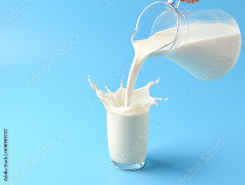 Pouring fresh milk into the glass with splashing on light blue background.