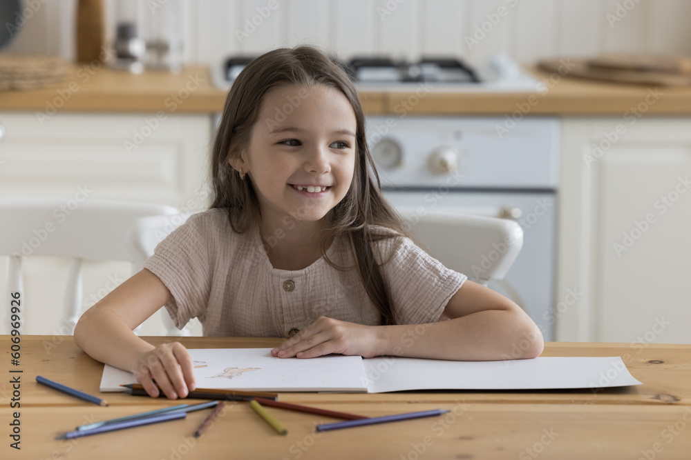 Happy joyful little kid drawing in coloring pencils in paper album at home, sitting at kitchen table, looking away, smiling, laughing. Kid engaged in learning game, developing creative artistic skills Happy joyful little kid drawing in coloring pencils in paper album at home, sitting at kitchen table, looking away, smiling, laughing. Kid engaged in learning game, developing creative artistic skills