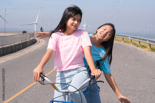 Two Young girl ride a bike on the road at the mountain with Wind Turbine, Khao Yai Thieng Electric Wind Turbine Thailand. photo