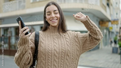 Young beautiful hispanic woman using smartphone dancing at street