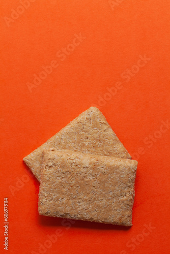 Two pieces of Indian mithai (dessert), delicate, soft, crunchy Gajak Bars made of Til, Desi Ghee, and Jaggery.  Top view. On orange background. photo