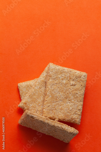 Three pieces of Indian mithai (dessert), delicate, soft, crunchy Gajak Bars made of Til, Desi Ghee, and Jaggery, on orang background. Top view. photo