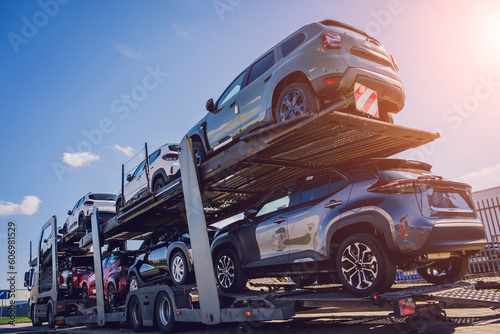 Car carrier trailer transports cars on highway at blue sky background.