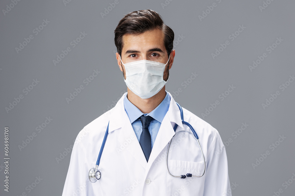 A male doctor in a white coat and medical mask and sterile gloves looks at the camera on a gray isolated background, copy space, space for text A male doctor in a white coat and medical mask and sterile gloves looks at the camera on a gray isolated background, copy space, space for text