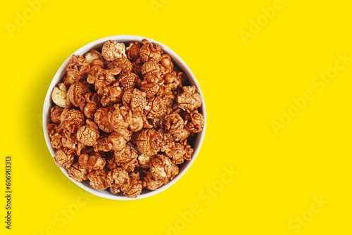 Chocolate caramel sweet popcorn in white bowl isolated on yellow background with clipping path. Top view.