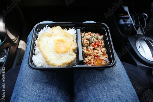 Steamed rice with fried egg and chicken basil in a plastic package placed on a woman's leg in the car.