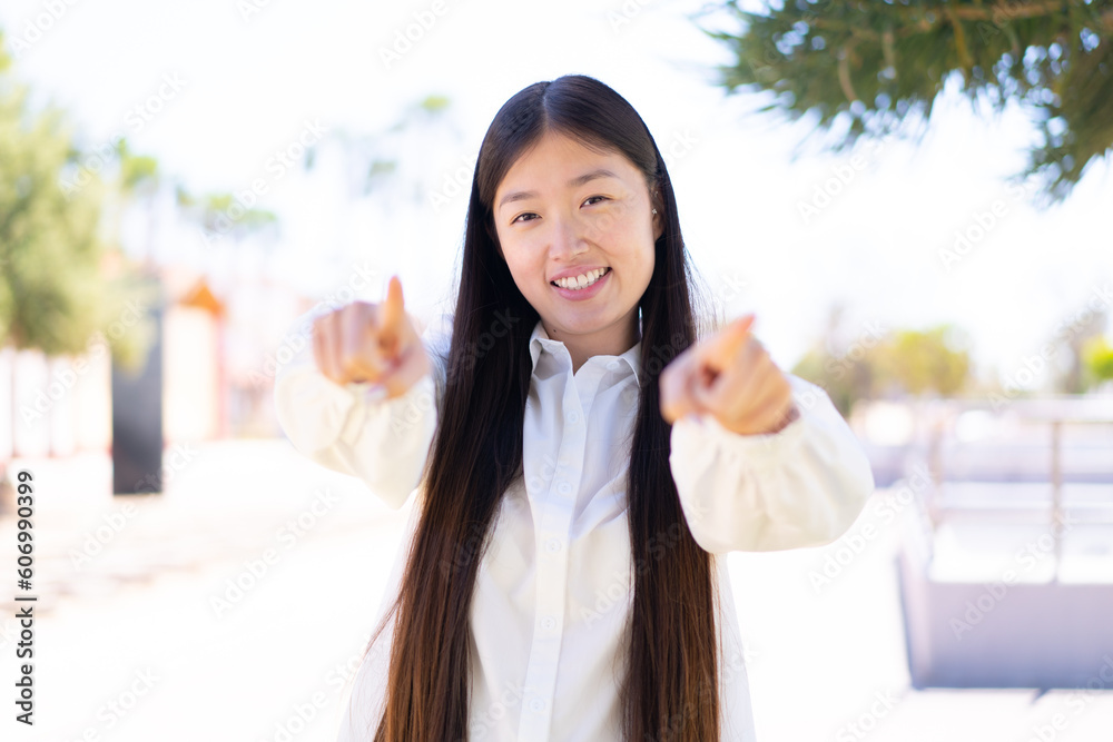 Pretty Chinese woman at outdoors points finger at you while smiling