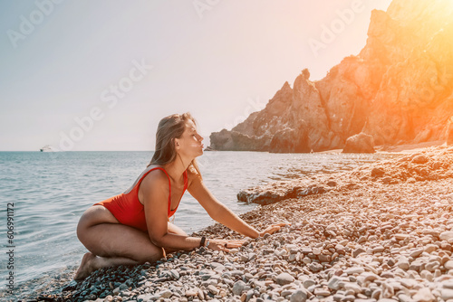 Young woman in red bikini on Beach. Girl lying on pebble beach and enjoying sun. Happy lady with long hair in bathing suit chilling and sunbathing by turquoise sea ocean on hot summer day. Close up © panophotograph