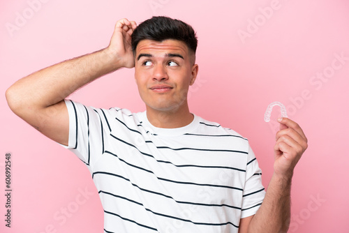 Young caucasian man holding invisaling isolated on pink background having doubts and with confuse face expression photo