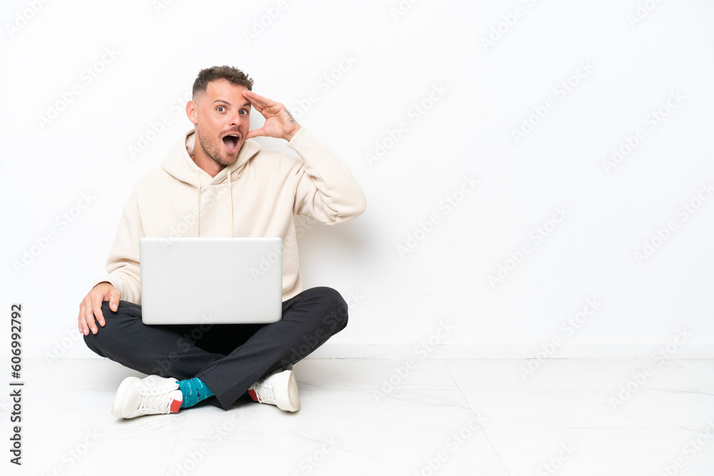 Young caucasian man with a laptop sitting on the floor isolated on white background with surprise and shocked facial expression Young caucasian man with a laptop sitting on the floor isolated on white background with surprise and shocked facial expression