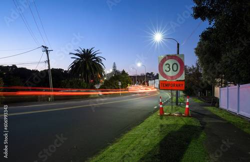 Obraz na płótnie Temporary 30km speed limit sign with traffic cones by the roadside. Car light trails on the road intersection. Auckland. w salonie