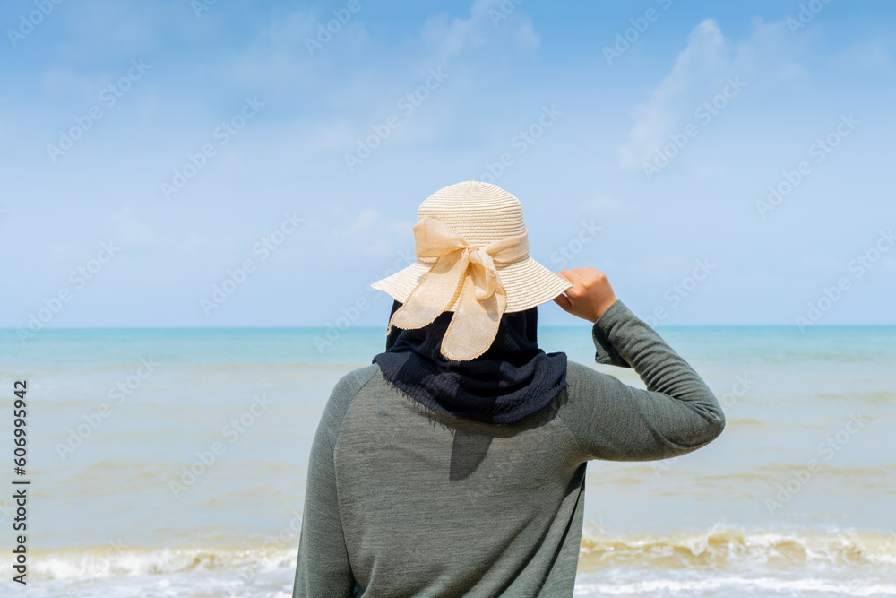 Happy Young muslim woman in grey dress and hat standing on the beach and open hands on sea with breaths a full breast and enjoys freedom.