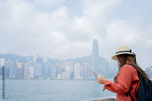 Asian tourist, cute woman with long hair are traveling in Hong Kong along with map and her camera with fun on her holiday,traveler relaxing and enjoying at Victoria harbour in Hong Kong.