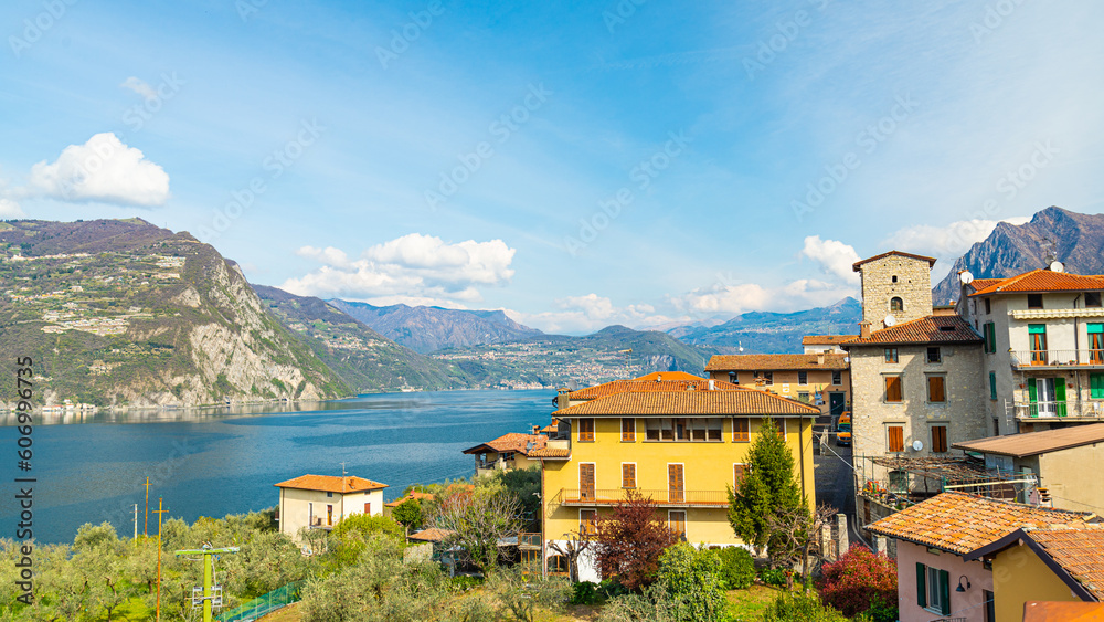 One of the traditional villages of Monte Isola (Mount Island), an island in the middle of the Lake Iseo, Italy. The blue waters of the lake on the left. Blue sky on the background.