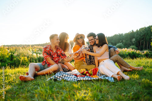 Group of young people gathered in garden for picnic. Friends have fun and drink beer. Vacation, picnic, friendship or holliday concept.