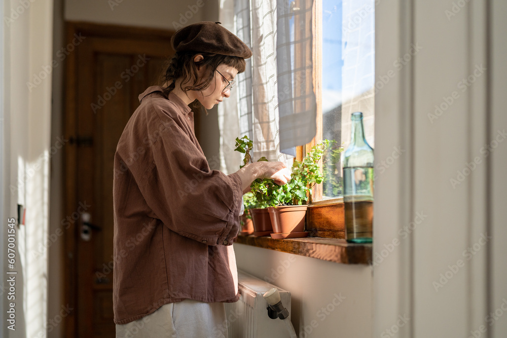 Hipster girl examining leaves of house plant, standing by window at home, visually inspecting indoor plants. Young woman checking houseplants for pests and damage Hipster girl examining leaves of house plant, standing by window at home, visually inspecting indoor plants. Young woman checking houseplants for pests and damage
