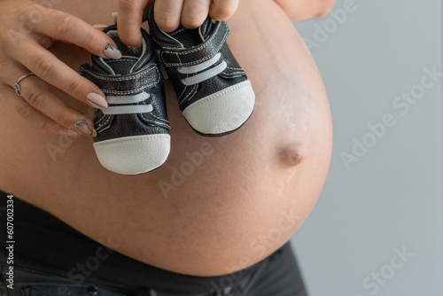 A young pregnant woman holding  baby shoes, against the backdrop of her pregnant belly. photo