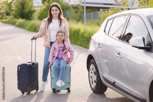 Family standing by the car with suitcases and waiting journey. Mom and daughter preparing for trip. Little girl sitting on kid suitcase.  © Aleksandr