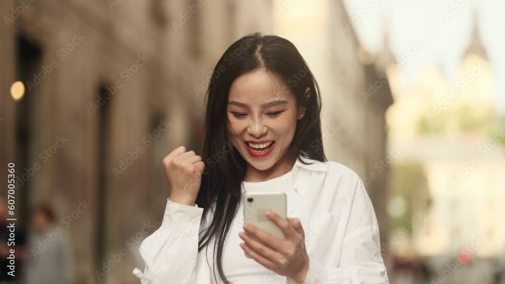 Pretty young asian woman walking in the city centre while get notification and celebrate online win success reading great news message feel amazed happy outdoors Triumph Lucky Wow concept Pretty young asian woman walking in the city centre while get notification and celebrate online win success reading great news message feel amazed happy outdoors Triumph Lucky Wow concept